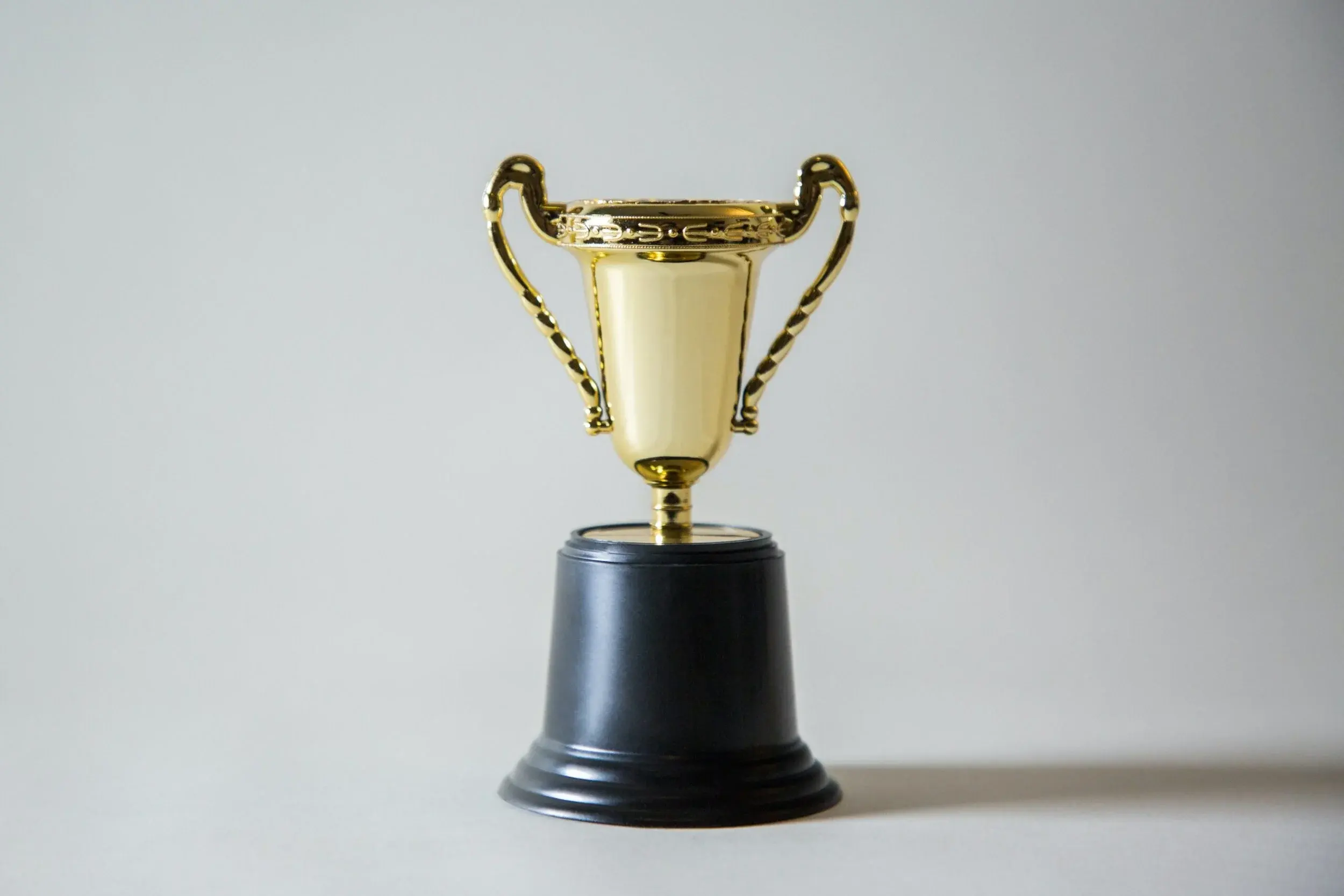 A small gold trophy on a black base against a plain grey background.