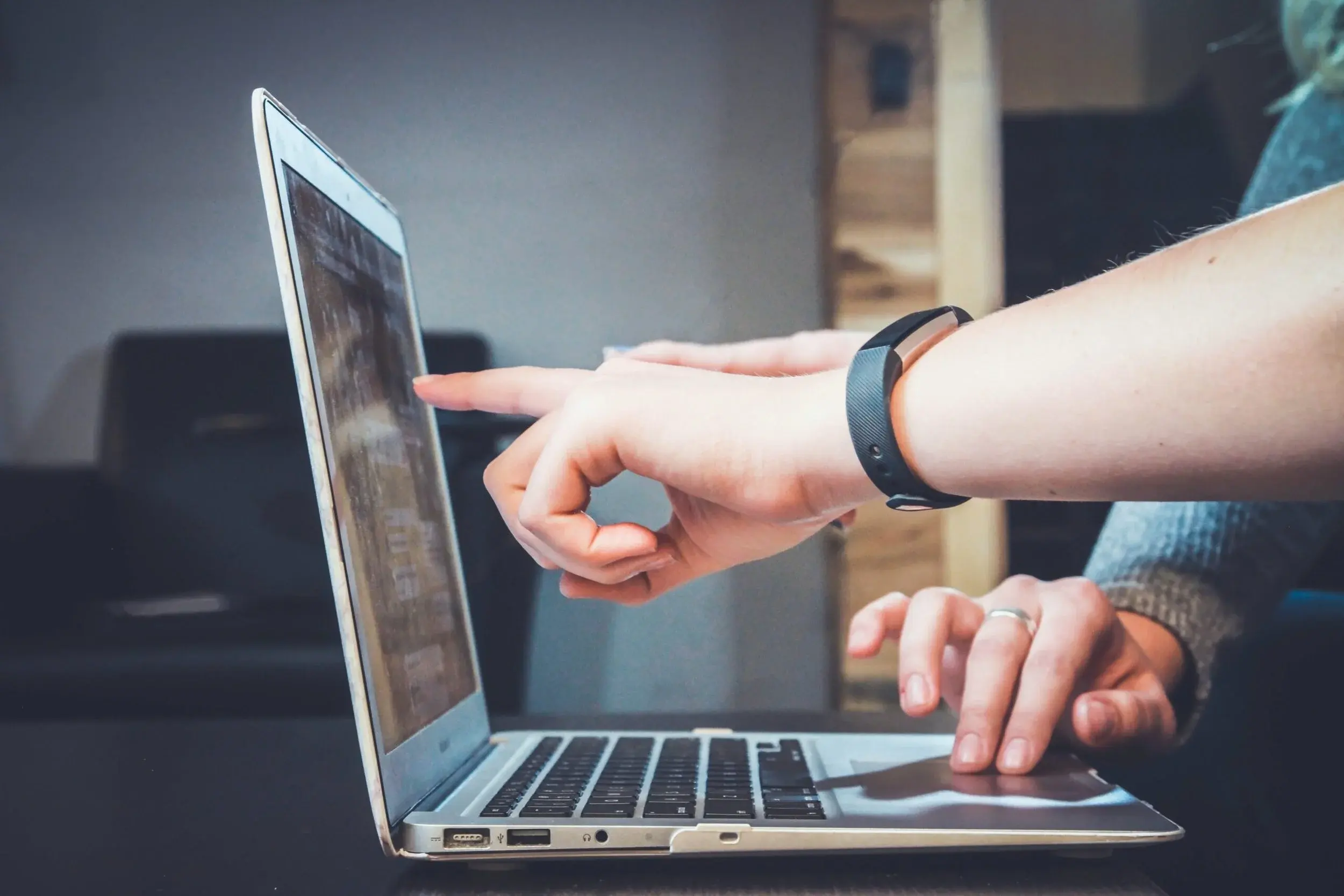 Two people at one laptop: one points at the screen while the other works the trackpad.