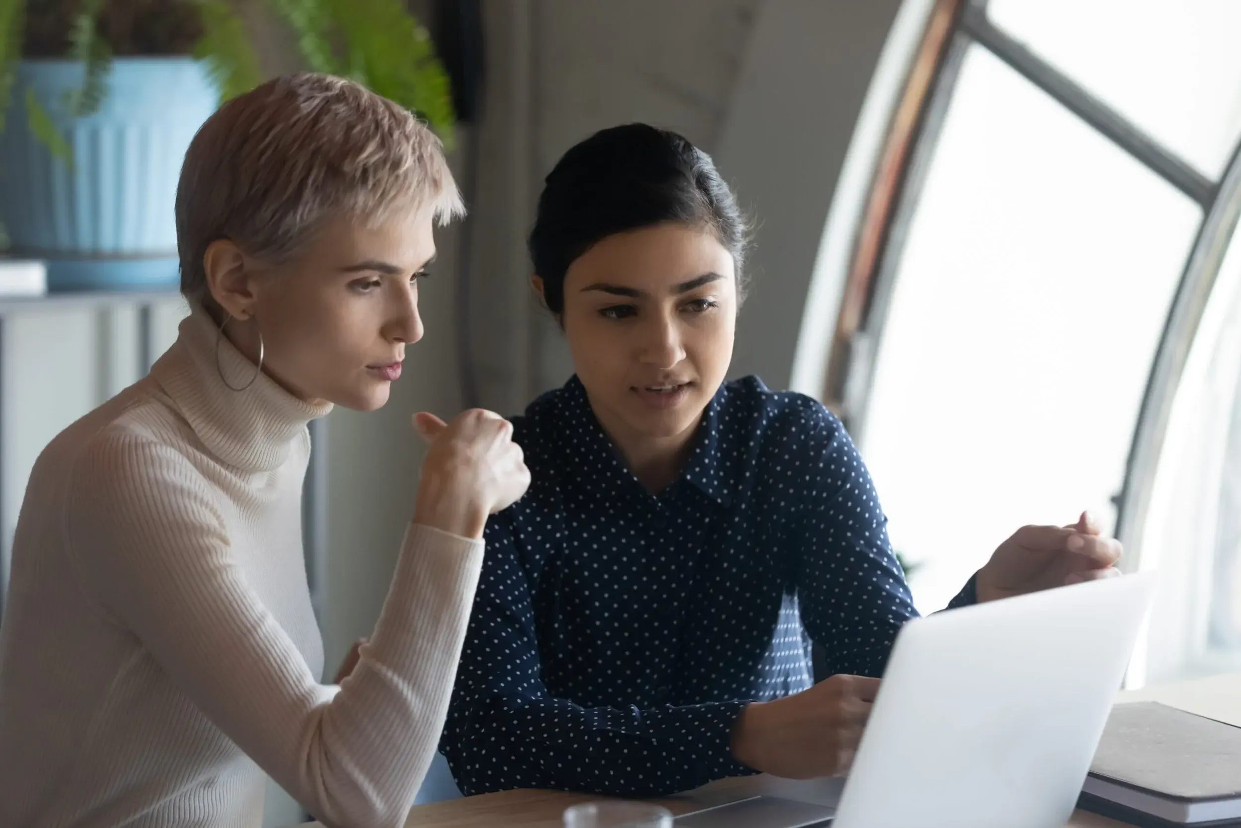 Two colleagues look at a laptop together while one explains something on screen.